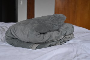 A blue and grey blanket sitting on top of a white bedspread. 